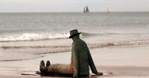 Bild sitzende Statue am Strand die gen Meer blickt